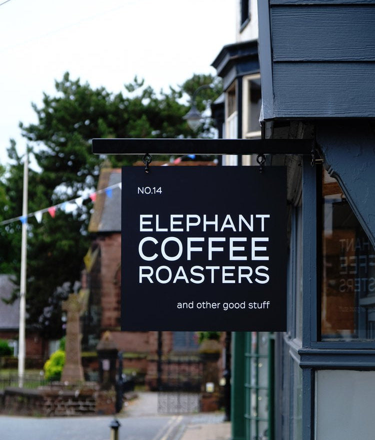 Sign for Elephant Coffee Roasters on a building exterior with trees and street in the background.